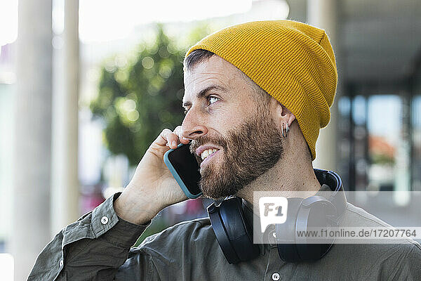 Modischer Mann mit Kopfhörern  der mit seinem Smartphone spricht  während er auf den Fußweg schaut
