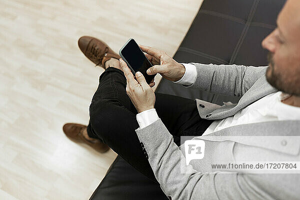 Male professional using smart phone while sitting on sofa in office