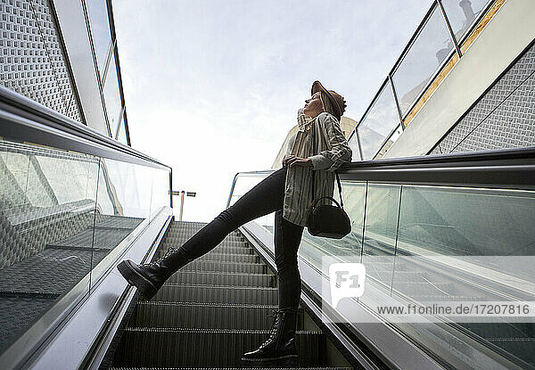 Frau lehnt sich auf der Rolltreppe an ein Geländer und steht gegen den Himmel