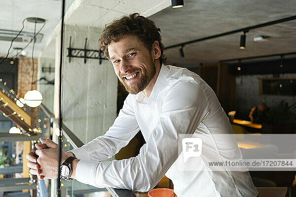 Lächelnder Geschäftsmann lehnt am Geländer eines Cafés