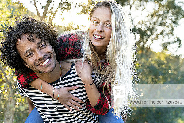 Playful woman piggybacking on man smiling while standing at front or back yard