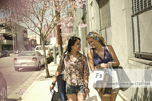 Happy female friends with shopping bags walking at sidewalk in city