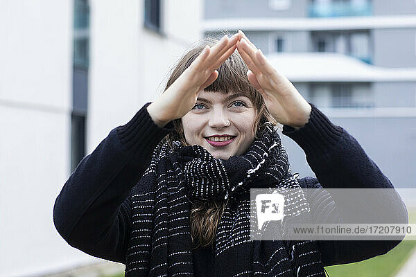 Smiling woman making hand sign while standing in city