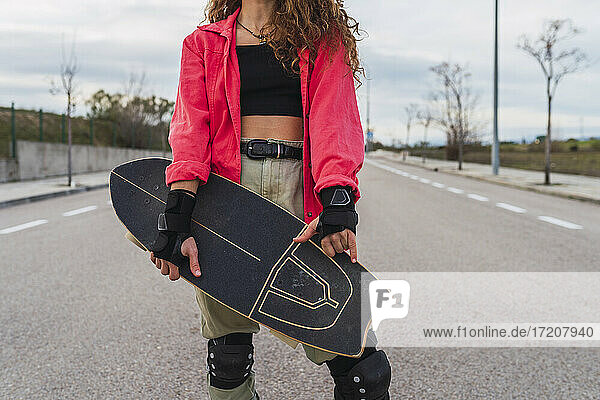 Frau mit fingerlosen Handschuhen gestikuliert  während sie ein Skateboard auf der Straße hält