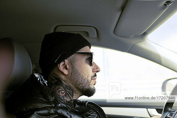 Tattooed man driving car while looking away