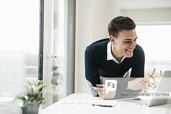 Smiling male professional leaning on chair while looking at laptop in home office