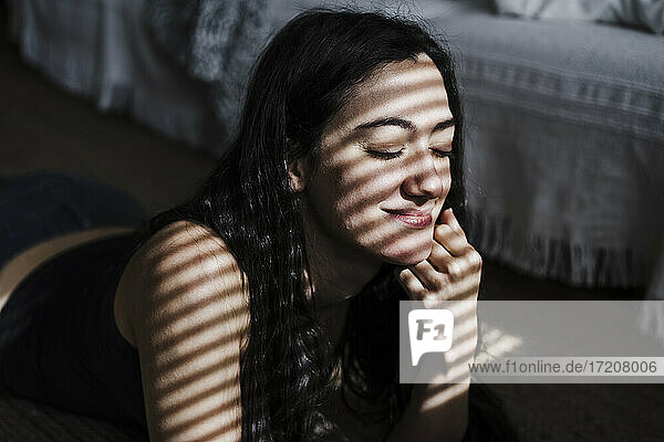 Lächelnde Frau mit Jalousien Schatten auf Gesicht liegend auf der Vorderseite im Wohnzimmer