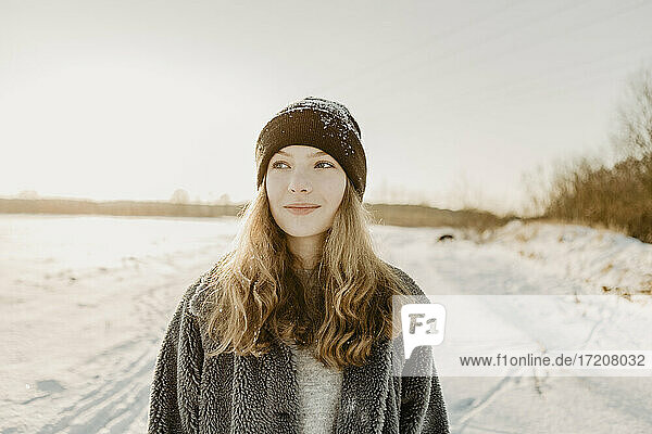 Portrait of beautiful teenage girl standing outdoors and smiling against rising winter sun