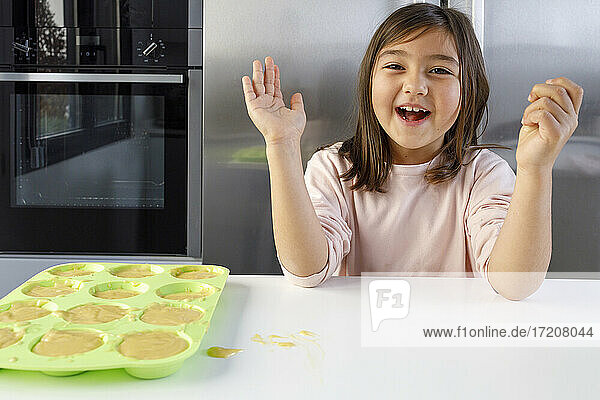 Lächelndes süßes Mädchen neben Muffinform auf Küchentisch