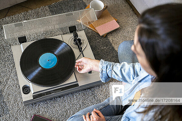 Frau spielt Schallplatte  während sie zu Hause auf dem Teppich sitzt