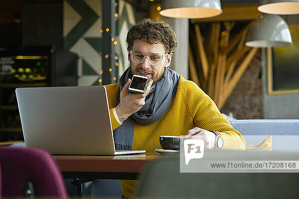 Businessman sending voice message through smart phone while having coffee at cafe