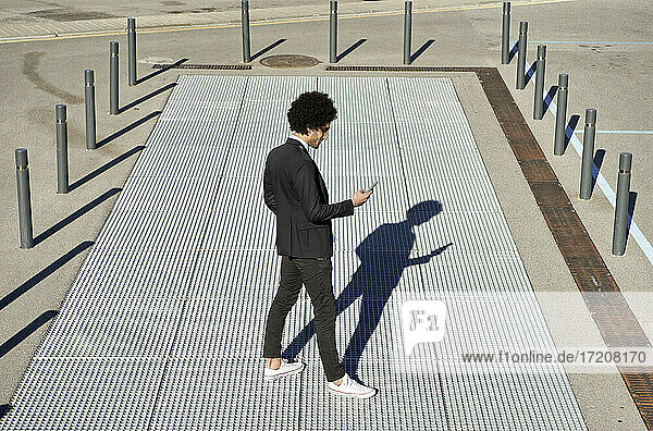 Männlicher Berufstätiger  der ein Smartphone benutzt  während er an einem sonnigen Tag auf dem Gehweg steht