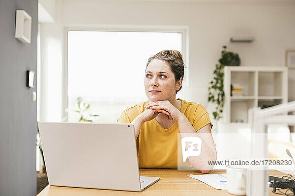 Nachdenkliche Unternehmerin sitzt mit Laptop am Schreibtisch und schaut weg