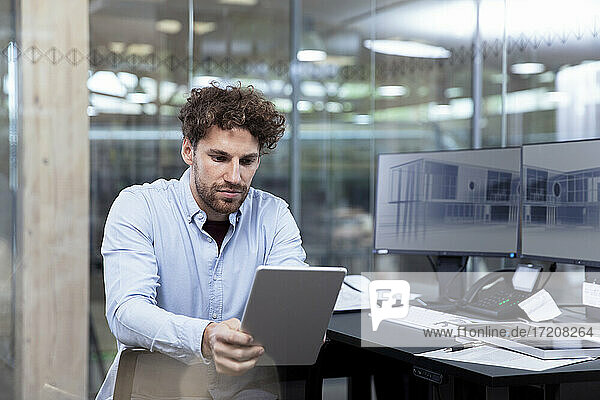 Young businessman using digital tablet while sitting at desk in office