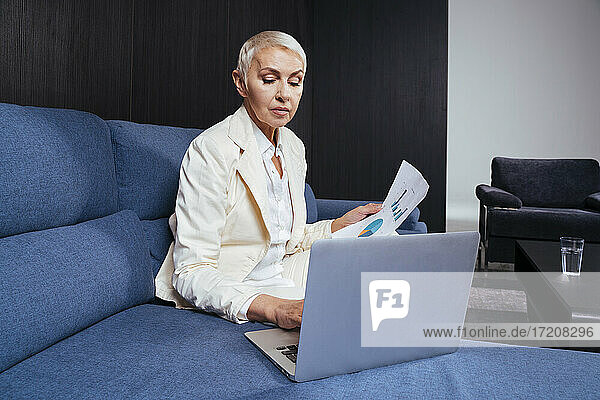 Businesswoman with document using laptop while working on sofa