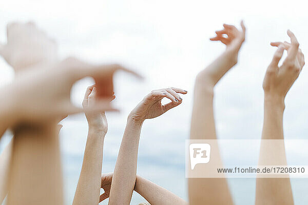 Female friends with raising arms against sky