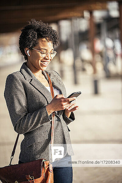 Lächelnde Frau  die auf dem Gehweg ein Mobiltelefon benutzt