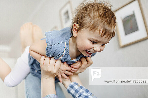 Playful mother lifting cheerful daughter while spending leisure time at home