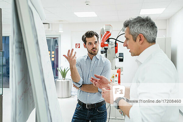 Male engineers gesturing while discussing business plans at white board in factory