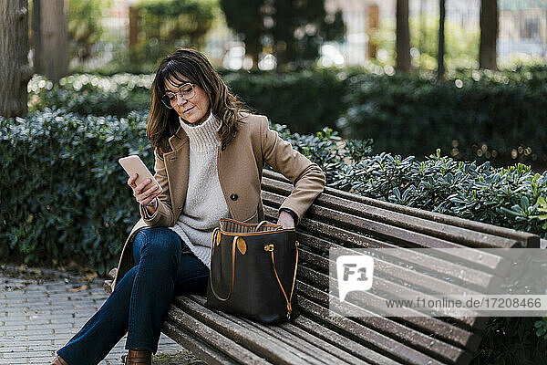 Reife Frau  die ihr Smartphone benutzt  während sie auf einer Bank im Park sitzt