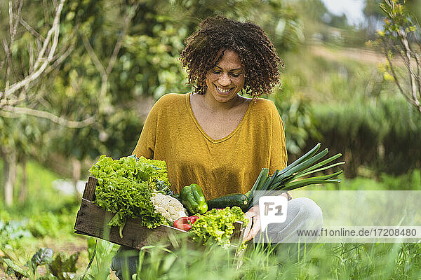 Lächelnde Frau betrachtet Gemüse in einer Kiste  während sie im Garten hockt
