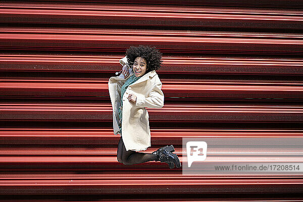 Glückliche Afro-Frau  die gegen einen roten Fensterladen springt