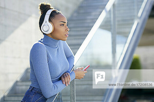 Junge Frau mit Kopfhörern  die wegschaut  während sie am Geländer steht