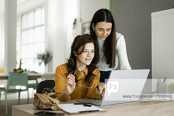 Lächelnde Tochter mit Mutter  die auf einen Laptop schaut  während sie an einem Schreibtisch im Büro zu Hause sitzen