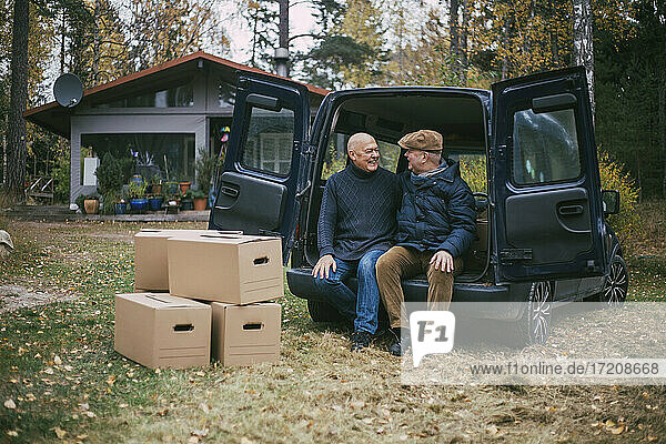 Glückliches homosexuelles Paar  das sich gegenseitig anschaut  während es im Kofferraum des Autos auf dem Hinterhof sitzt