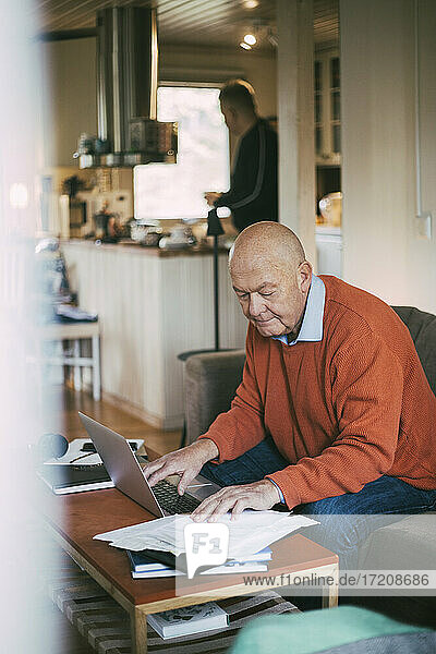 Elderly gay man using laptop while calculating financial bill at home