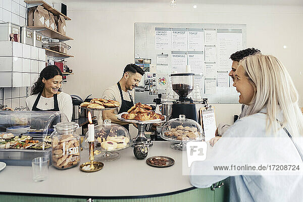 Smiling customers looking at male and female owners at delicatessen store