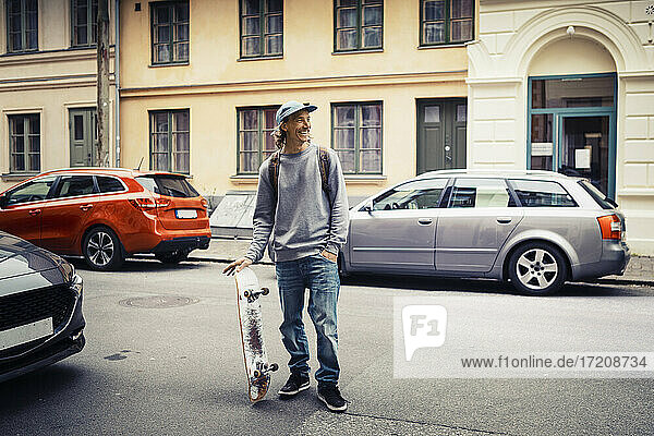Männlicher Skateboarder mit Hand in der Tasche schaut weg  während er auf der Straße steht