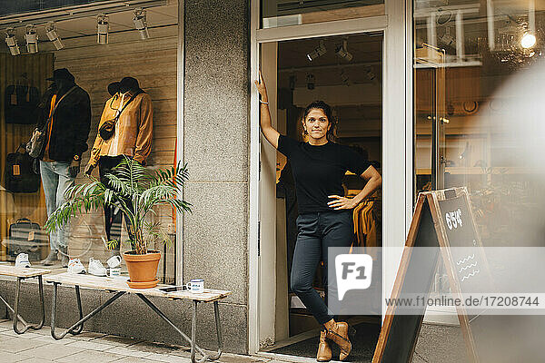 Weibliche Unternehmerin mit Hand auf der Hüfte stehend in der Tür eines Einzelhandelsgeschäfts