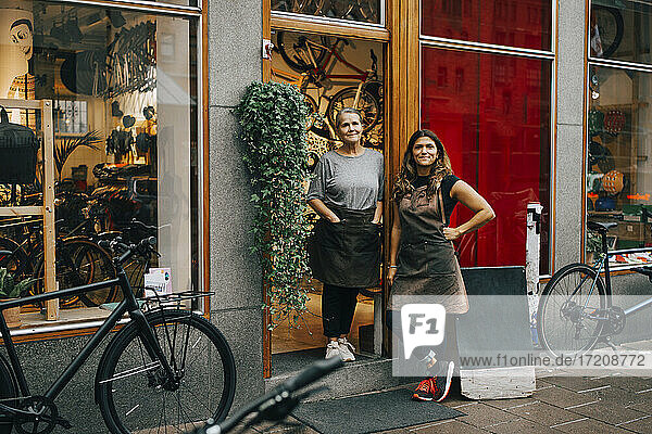 Lächelnde weibliche Mitarbeiter stehen vor der Tür eines Fahrradladens