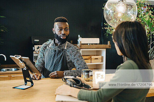 Männlicher Besitzer im Gespräch mit weiblichem Kunden im Café