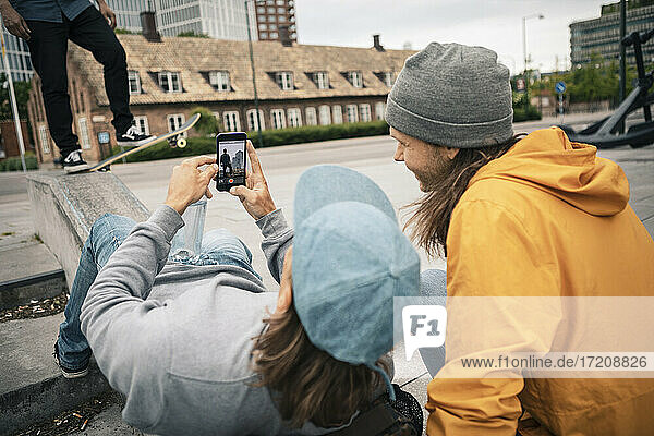 Freunde fotografieren durch Handy während männlicher Skater mit Skateboard auf Stützmauer
