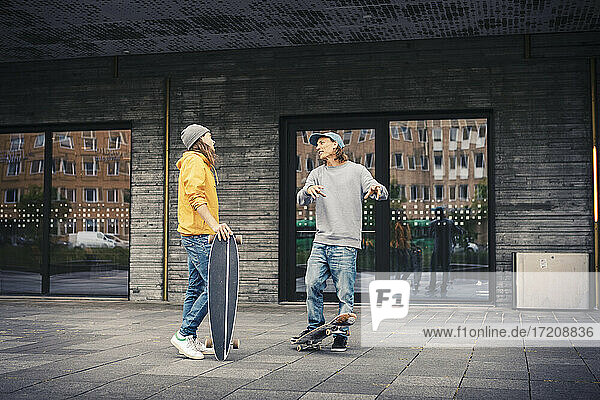 Männliche Freunde unterhalten sich  während sie mit Skateboard auf dem Fußweg stehen