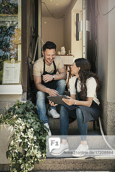 Lächelnde weibliche und männliche Besitzer mit digitalem Tablet diskutieren auf den Stufen eines Cafés
