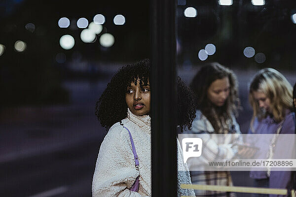 Afrikanische Teenager-Mädchen schauen  während sie mit weiblichen Freunden an der Bushaltestelle stehen