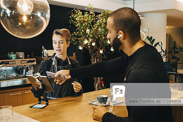 Männlicher Kunde beim kontaktlosen Bezahlen mit dem Smartphone in einem Coffee Shop