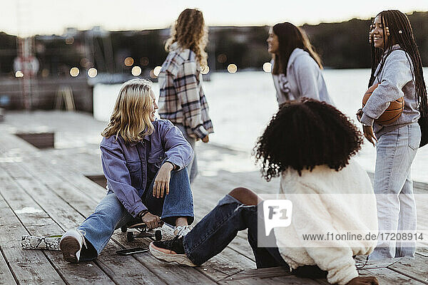 Glückliche weibliche Freunde verbringen Freizeit auf Pier während Sonnenuntergang