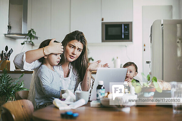 Mutter mit Kindern bei der Online-Beratung per Videoanruf in der Küche