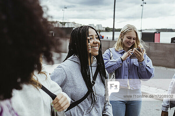 Teenager-Mädchen mit Smartphone stehend mit Freundinnen auf dem Fußweg