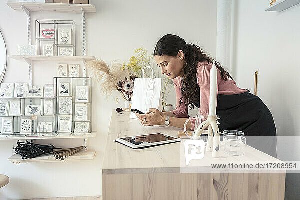 Weiblicher Besitzer  der ein Smartphone benutzt  während er sich auf einen Tisch im Designstudio stützt