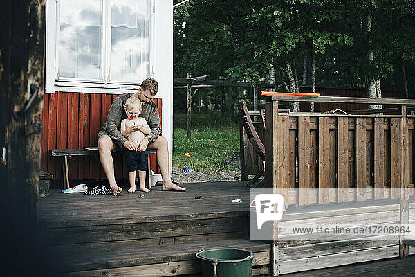 Father looking at son while sitting on bench during summer