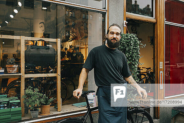 Portrait of smiling male mechanic by bicycle outside retail shop