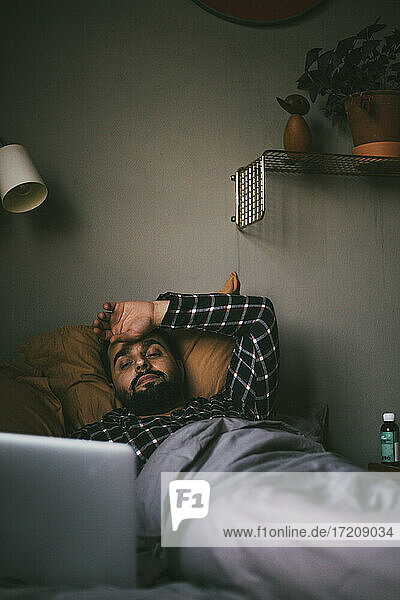 Kranker Mann mit Online-Konsultation auf Laptop  während er auf dem Bett liegt