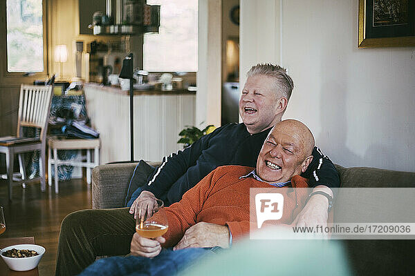 Cheerful gay couple laughing while sitting on sofa in living room