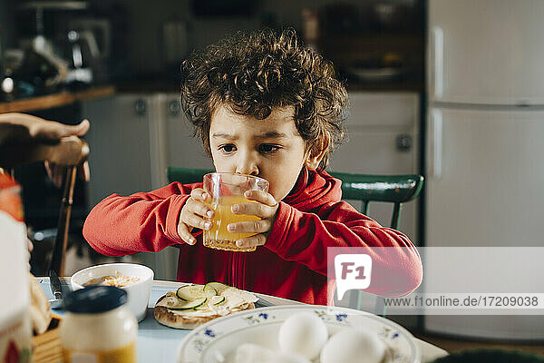 Cute boy drinking juice while sitting by table during breakfast