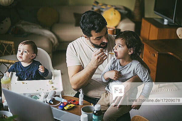 Father feeding son at table in living room